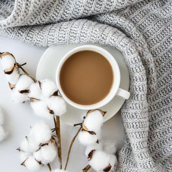 Cup of coffee with cotton plant cinnamon sticks and anise star on white background. Sweater around. Winter morning routine. Coffee break. Copy space. Top view. Breakfast. Flat lay