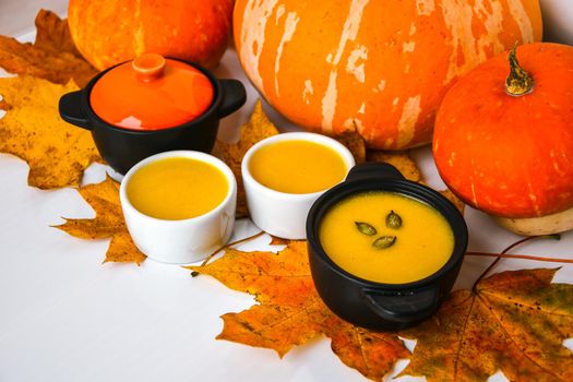 Autumn food. Pumpkin puree soup, leaves. Autumn harvest, pumpkins, leaves on grey as abstract background. Thanksgiving day. Seasonal food. Vegetarian