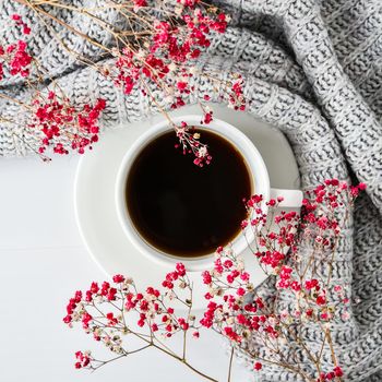 Cup of black coffee on white background with sweater and bright pink flowers. Flat lay. Copy space. Fashion concept. Cozy lifestyle. Still life