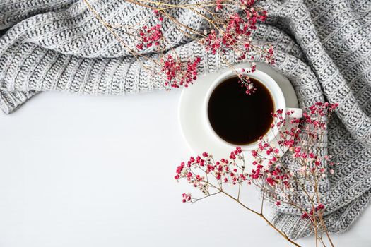 Cup of black coffee on white background with sweater and bright pink flowers. Flat lay. Copy space. Fashion concept. Cozy lifestyle. Still life