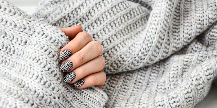 Hand in sweater with zebra animal printed nails. Female manicure. Glamorous beautiful manicure. Manicure salon concept. Nail polish close up.