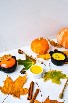 Autumn food. Pumpkin puree soup, leaves. Autumn harvest, pumpkins, leaves on grey as abstract background. Thanksgiving day. Seasonal food. Vegetarian