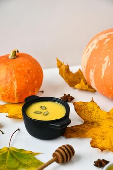 Autumn food. Pumpkin puree soup, leaves. Autumn harvest, pumpkins, leaves on grey as abstract background. Thanksgiving day. Seasonal food. Vegetarian