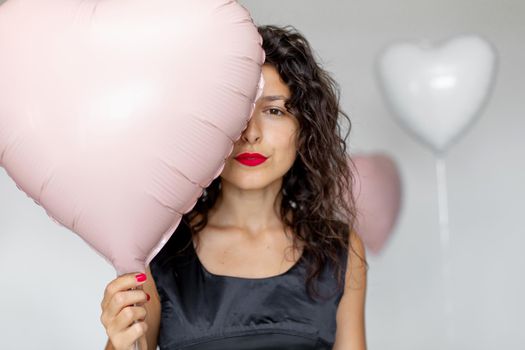 Sexy brunette girl posing with heart-shaped balloons on a white background.