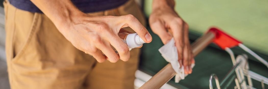 Man hand disinfecting shopping cart with alcohol spray for corona virus or Covid-19 protection. BANNER, LONG FORMAT