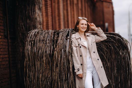 A happy stylish girl in a gray coat walks around the city.