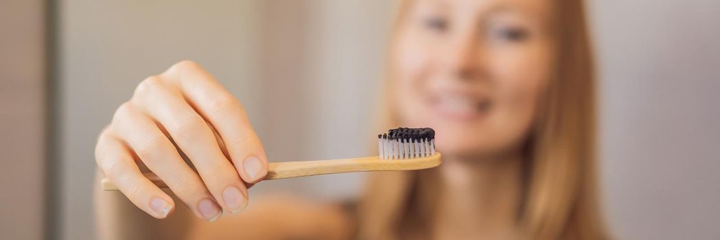 young woman brushing her teeth with a black tooth paste with active charcoal, and black tooth brush in her bathroom. BANNER, LONG FORMAT