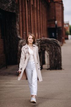 A happy stylish girl in a gray coat walks around the city.