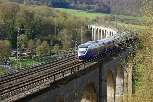 A train is speeding over an old railway viaduct. It is a 482 metres long and up to 35 metres high and made out of limestone in 1853.  It spans a valley west of the town of Altenbeken. 