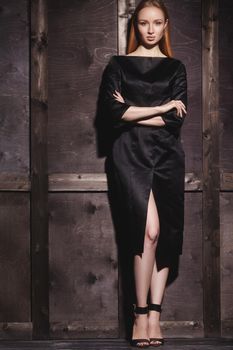Fashion portrait of beautiful young woman in sexy black dress near with wood wall. Elegant dark evening look.