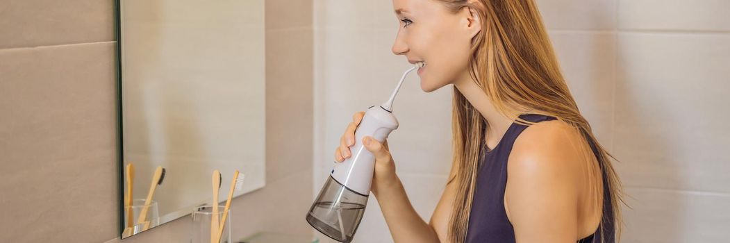 Woman using an oral irrigator in bathroom. BANNER, LONG FORMAT