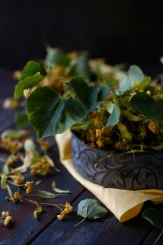 Fresh harvested flowers and leaves of linden tree in vintage mental bowl with yellow cloth.