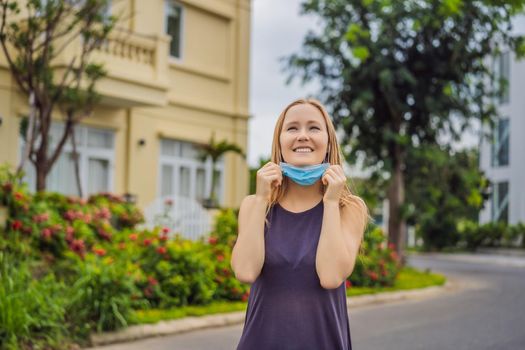 Quarantine is over concept. Woman taking off mask against the background of small town houses. We are safe. Coronavirus ended. We won. No more quarantine. Breathe deep. Take off the mask. Coronavirus is over.