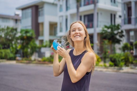 Quarantine is over concept. Woman taking off mask against the background of small town houses. We are safe. Coronavirus ended. We won. No more quarantine. Breathe deep. Take off the mask. Coronavirus is over.