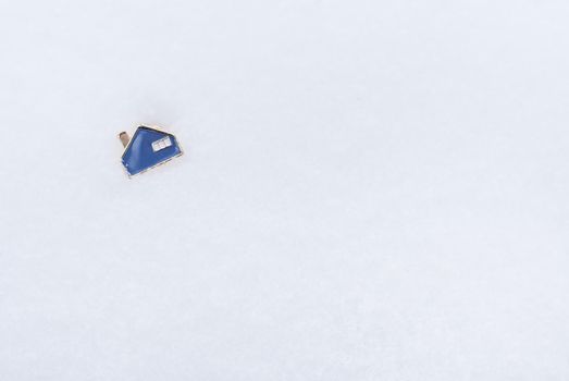 A metal small blue house that lies on the snow. Place for an inscription. Real estate and mortgage concept