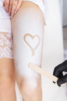 Professional cosmetology, body epilation, leg hair removal concepts. Shugaring, laser hair removal. Legs of a client in cream with a heart on her leg