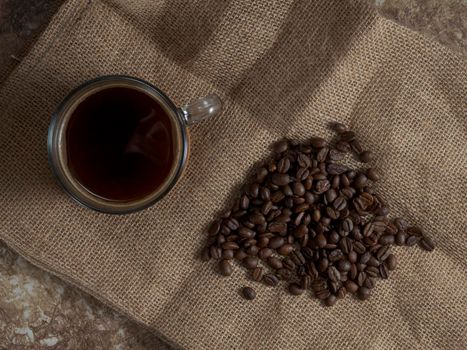 dark roasted coffee beans on burlap and a mug of freshly brewed natural coffee.