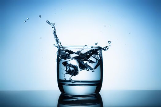 Ice cubes splashing into glass of water.