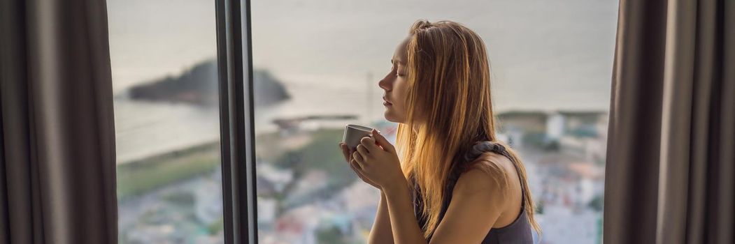Young woman is drinking coffee in the morning on the background of a window with a sea view. BANNER, LONG FORMAT