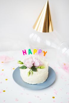 A very beautiful small white cake, decorated with fresh eustoma flowers against the background of sweets and the inscription happy birthday, balloons, hats. Holiday concept