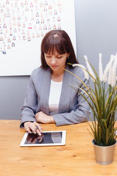 A brunette businesswoman in a gray jacket at her desk with a tablet in her hands. Business portrait in the office.