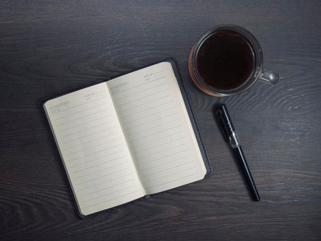 Workplace with notebook, pen and glass coffee mug on wooden background.