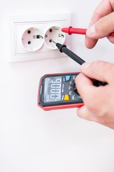 Measuring the voltage in the socket with a professional digital multimeter. Profession electrician, the process of installing sockets. Close-up, selective focus, noise