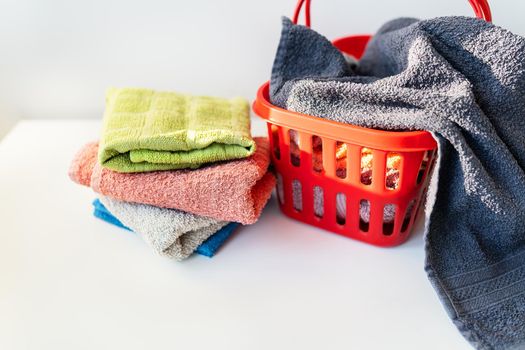 Multi-colored towels lie in a red laundry basket on a white background. Washing and ironing clothes, top view.