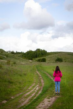 A woman in a pink raincoat looks at a mountain road. The concept of hiking in the mountains, trekking, outdoor recreation