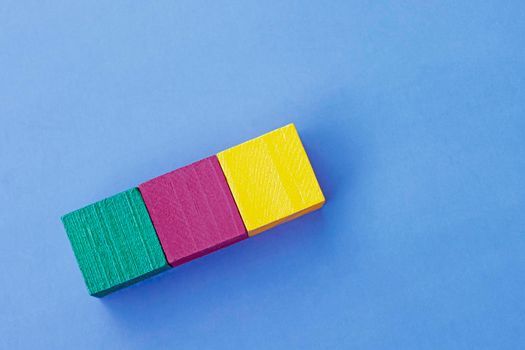 Three colorful wooden cubes against blue background. Flat lay. Copy Space. Directly above.