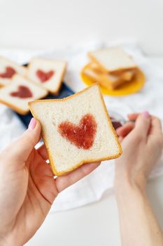 The girl makes a toast on which the heart is made of jam. Surprise breakfast concept in bed. Romance for St. Valentine's Day