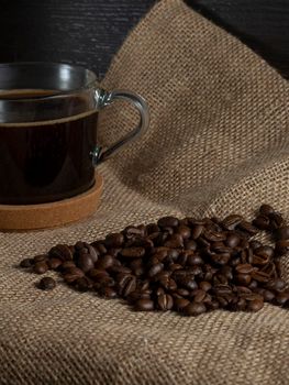 dark roasted coffee beans on burlap and a mug of freshly brewed natural coffee.