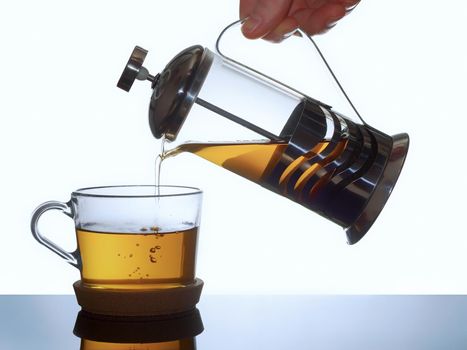 Transparent glass mug and french press with warm tea on a light background.