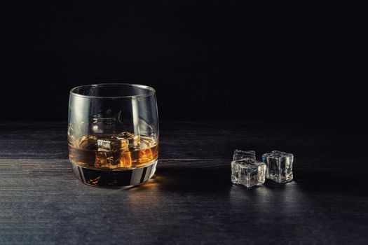 Whiskey splash in a glass with ice on a wooden table.