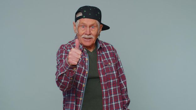 Great job, nice. Cheerful positive happy senior man showing thumbs up and nodding in approval, successful good work. Elderly stylish one grandfather on gray studio background. People sincere emotions