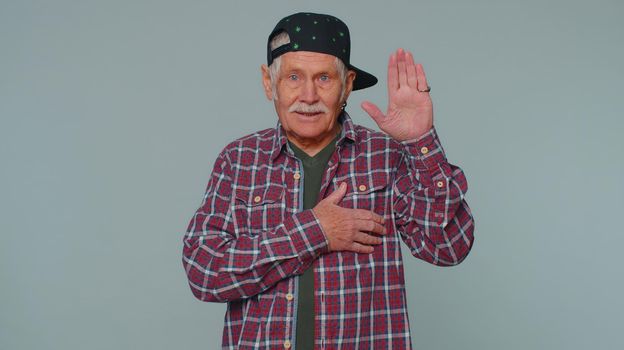 I swear to be honest. Sincere responsible senior man raising hand to take oath, promising to be honest and to tell truth, keeping hand on chest. Elderly grandfather isolated on gray studio background