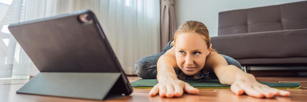 Fitness woman exercising on the floor at home and watching fitness videos in a tablet. People do sports online because of the coronovirus. BANNER, LONG FORMAT