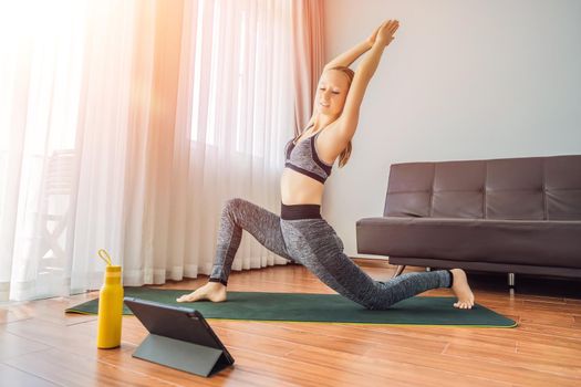 Fitness woman exercising on the floor at home and watching fitness videos in a tablet. People do sports online because of the coronovirus.