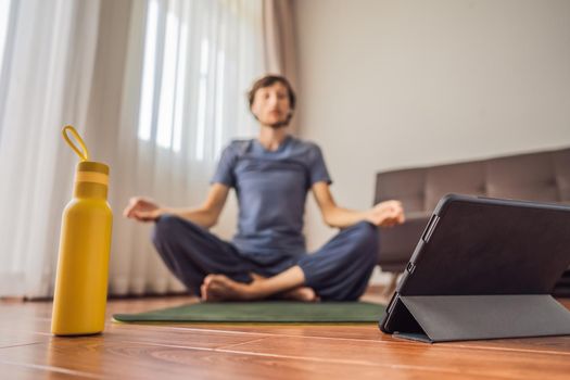 Fitness man exercising on the floor at home and watching fitness videos in a tablet. People do sports online because of the coronovirus. Focus on the tablet.
