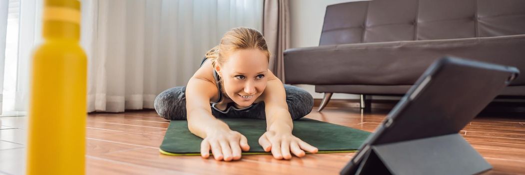 Fitness woman exercising on the floor at home and watching fitness videos in a tablet. People do sports online because of the coronovirus. BANNER, LONG FORMAT