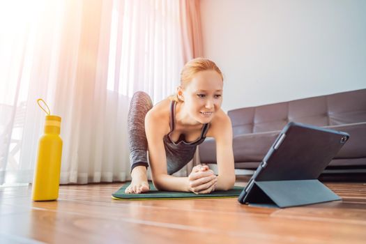 Fitness woman exercising on the floor at home and watching fitness videos in a tablet. People do sports online because of the coronovirus.