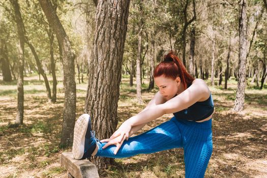 young woman practicing stretching exercises to gain flexibility outdoors. sporty woman preparing for a marathon. health and wellness lifestyle. Natural sunlight, background of natural vegetation, forest, sportswear.