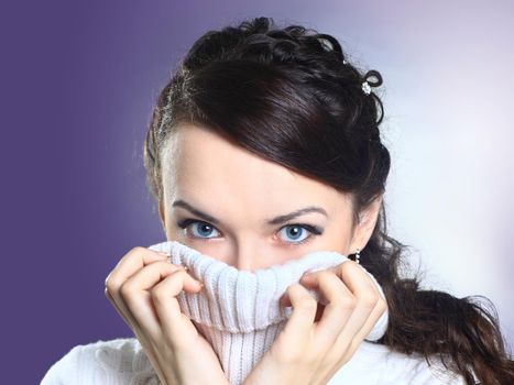 Beautiful girl in sweater buries her face. Isolated on a purple background.