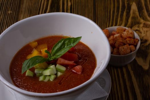 Raw tomato soup, typical food of Spain, served in white bowls with pieces of tomato, cucumber and paprika. Wooden background.