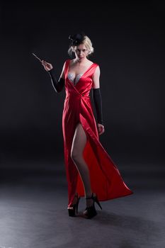 Beautiful young girl in a red dress with a cigarette, in cabaret style, isolated on a dark background.