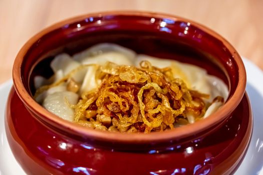 Russian and ukrainian cuisine. Dumplings with potatoes and fried onion in a pot on an old wooden background. Boiled dough with filling. Spoon. Rustic. Background image, copy space.