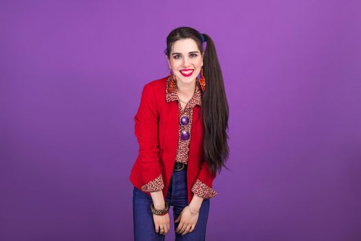 Happy laughing young brunette woman in 90s style in red jacket on purple background.