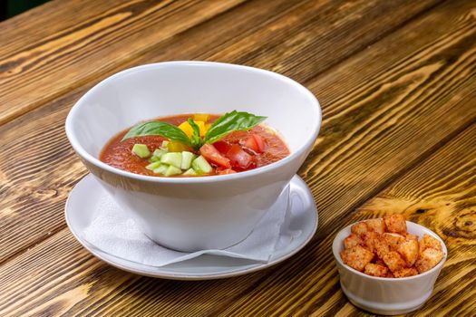 Raw tomato soup, typical food of Spain, served in white bowls with pieces of tomato, cucumber and paprika. Wooden background.