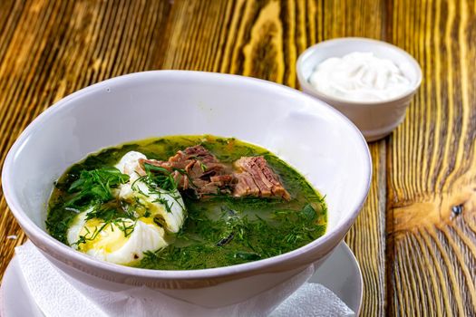 Green Sorrel soup with with boiled eggs wedges in white bowl. Selective focus, bunch of fresh sorrel on background.
