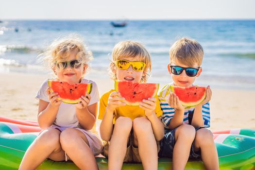 Coronavirus is over. Quarantine weakened. Take off the mask. Now you can travel. Children eat watermelon on the beach in sunglasses.